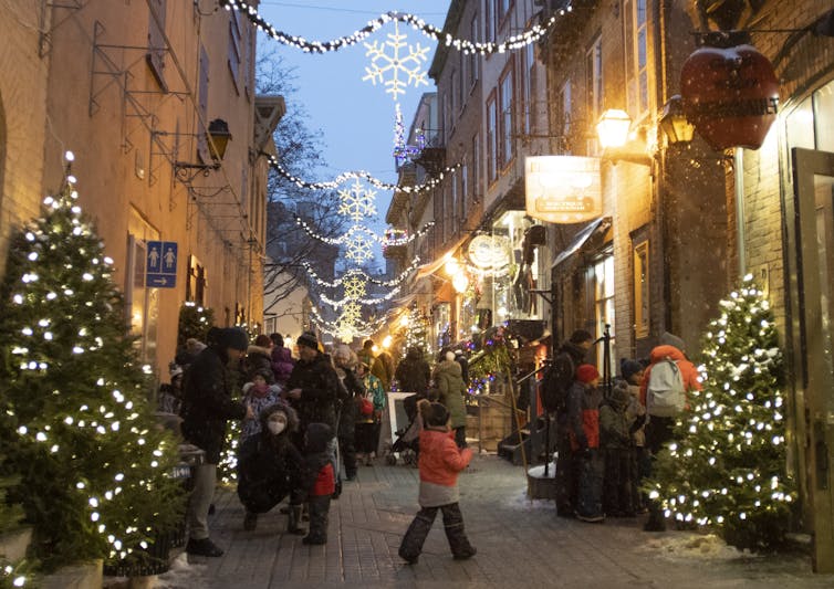 people walk on a wintry street festooned with christmas decorations anda lighting.