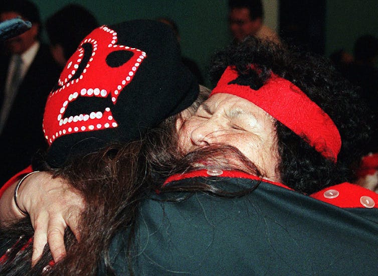 Two people wearing Indigenous clothing hug