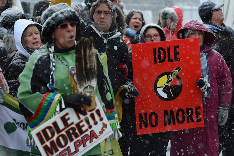 People wearing winter clothing carry signs that read: Idle No More