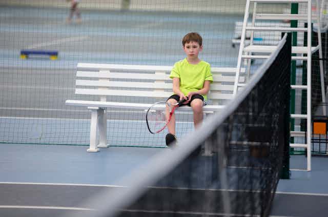 A sad boy holds a tennis racket.