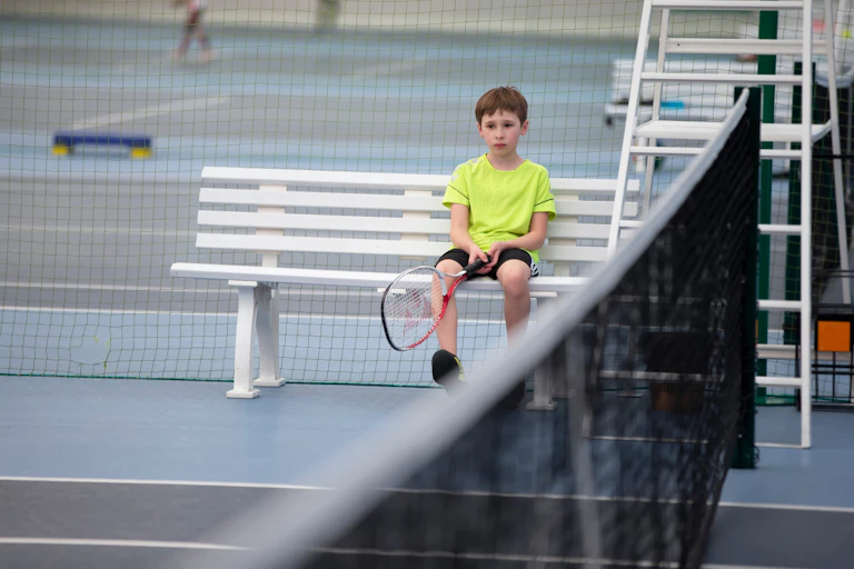 A sad boy holds a tennis racket.