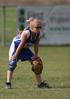 A girl stands on the field in a softball game.