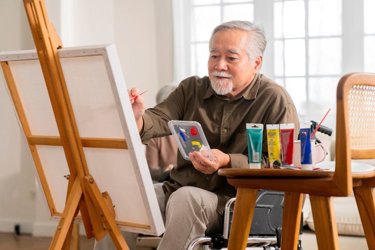 An elderly man in a wheelchair paints.