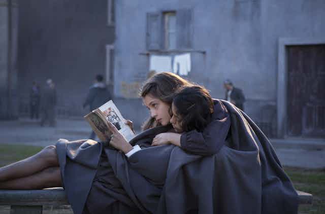 two girls in school uniforms lay on a bench, reading