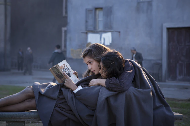 two girls in school uniforms lay on a bench, reading