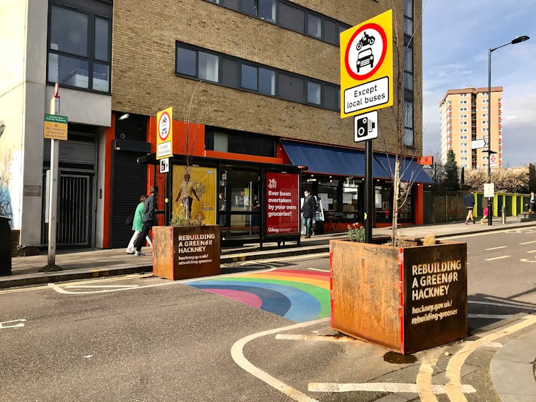 A rainbow painted on a street surface with planters restricting access to the road.