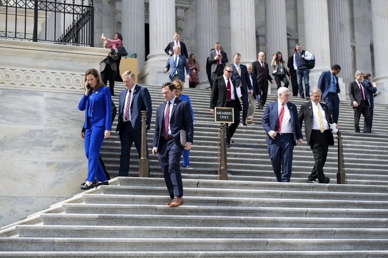 Un grupo de personas bajando las escaleras del edificio del Capitolio de los Estados Unidos en un día soleado.