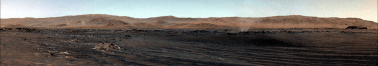 Reddish and brown desert landscape with several plumes of dust rising from it.