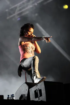 Ms Dynamite wears her hair in a punky braid, and stands one leg on an amp as she performs.