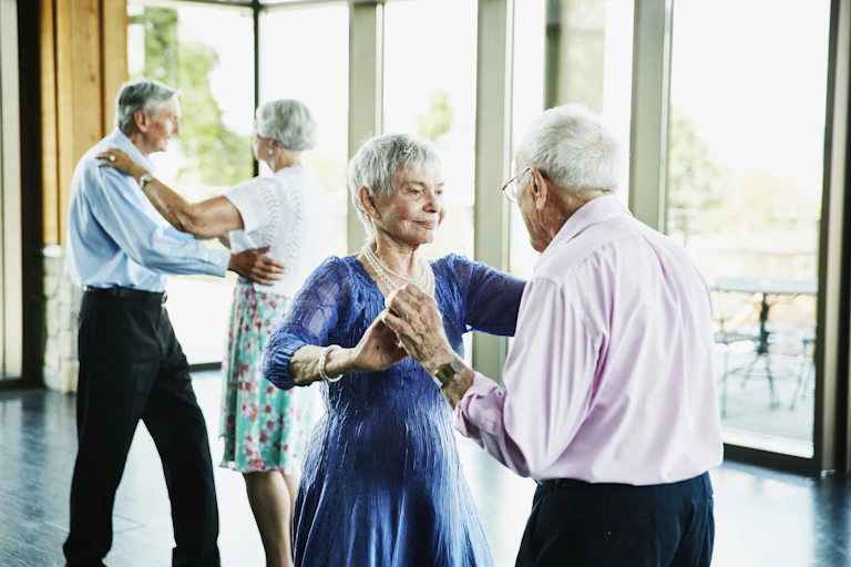 Two well-dressed elderly couples engage in ballroom dancing.