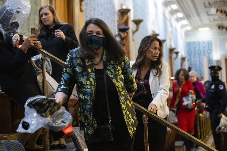 Several women looking afraid trying to leave a large, high-ceilinged room.
