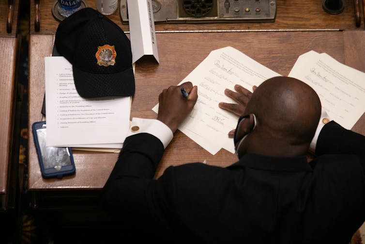 A man in a suit at a desk signs a paper.