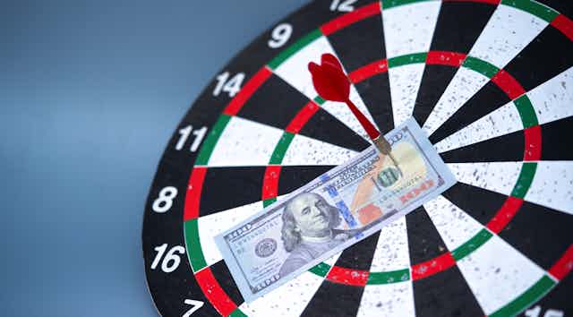 a $100 bill is stuck to a dartboard with a dart sticking in it