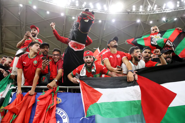 A group of people in a stadium, waving red, green, black and white flags, a mascot in a horse outfit among them.