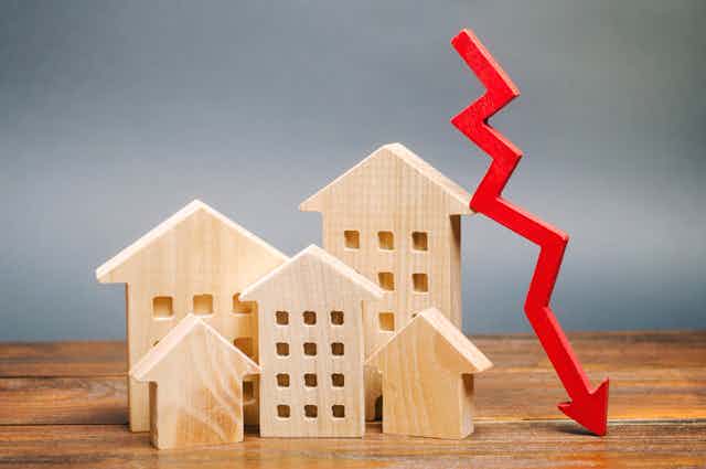 Miniature wooden houses on a table next to a red arrow going down.