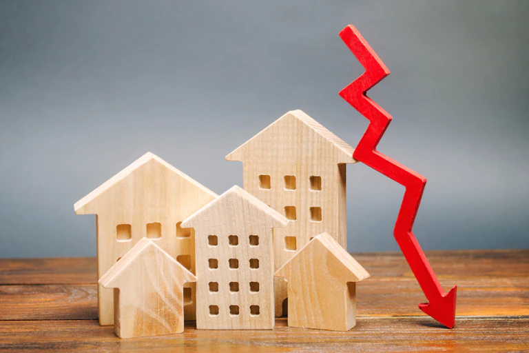 Miniature wooden houses on a table next to a red arrow going down.