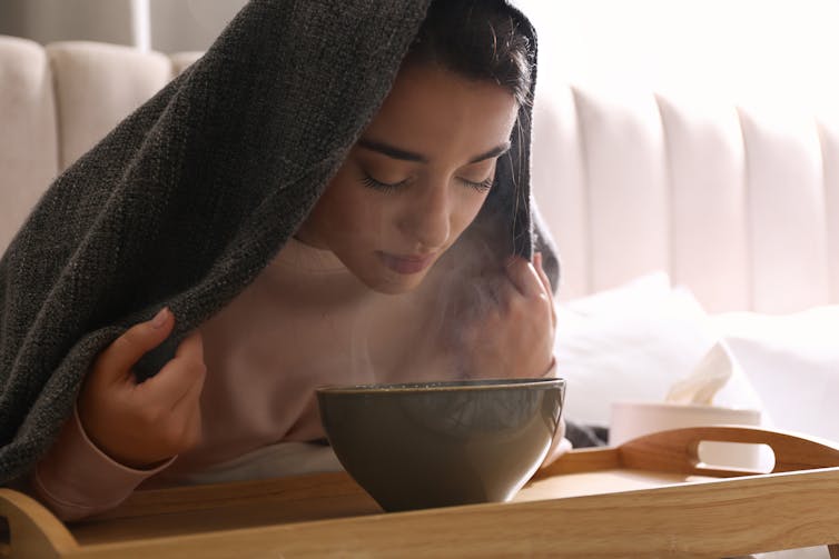 A woman with her face over a bowl.