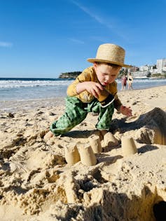 A young bots plays with a takeaway cup, making moulds on the beach.