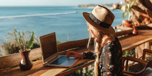 Woman with laptop on bench overlooking the ocean.