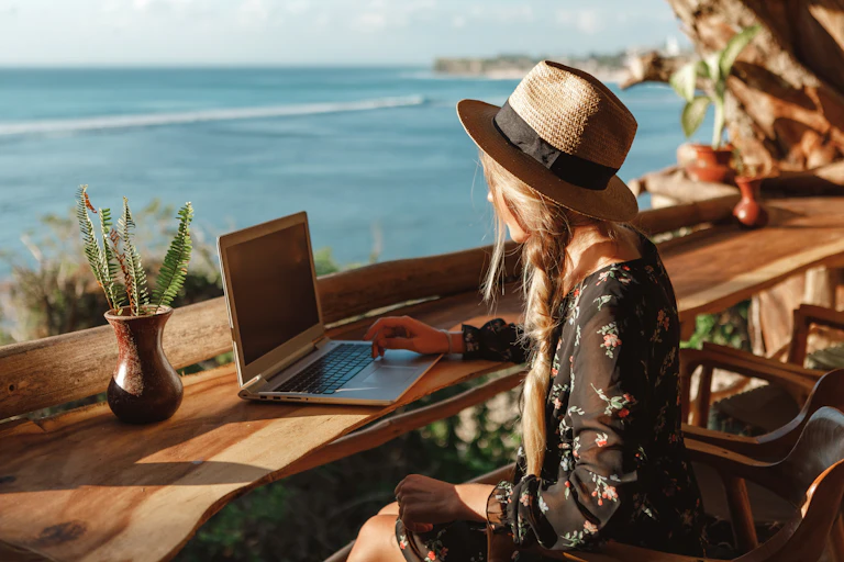 Woman with laptop on bench overlooking the ocean.