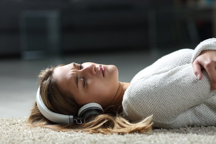 Young woman lying on the floor, with headphones on.