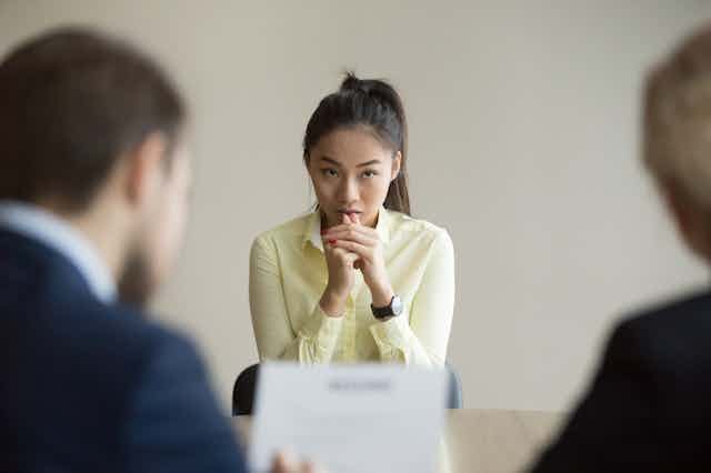 A person sits with two people in an interview.