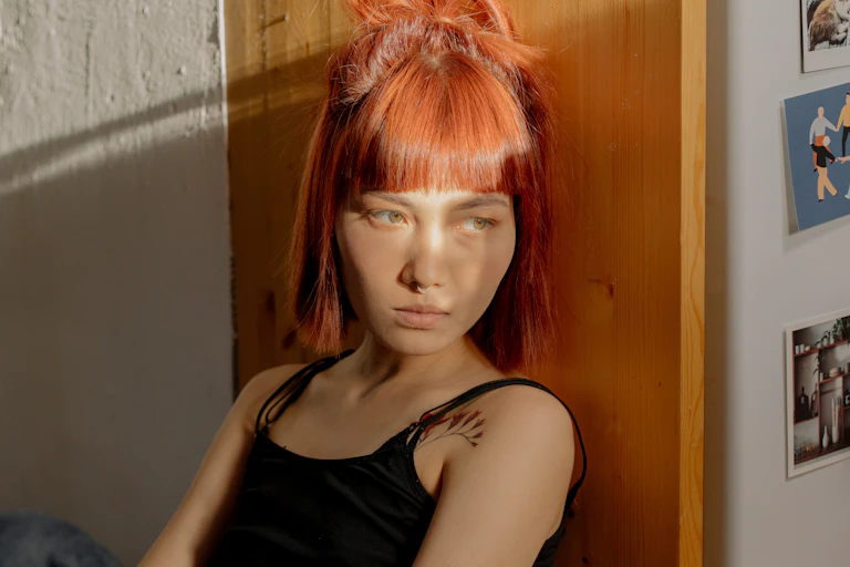 A young woman leans on a wall, with a sad expression