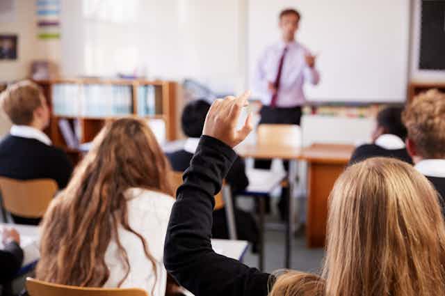 A teacher calls on a student who is raising her hand.