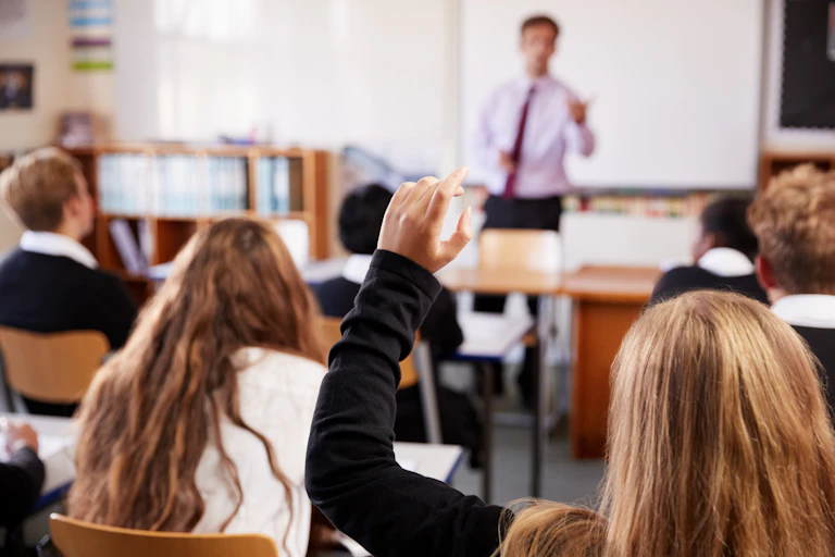 A teacher calls on a student who is raising her hand.