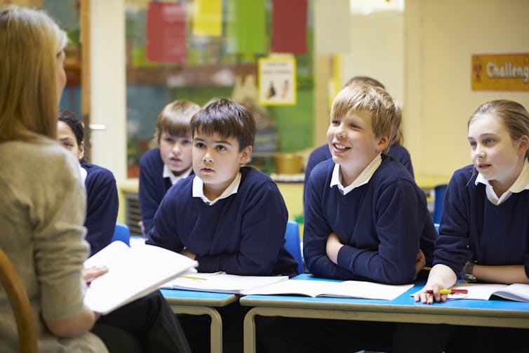 A teacher speaks while primary students listen.