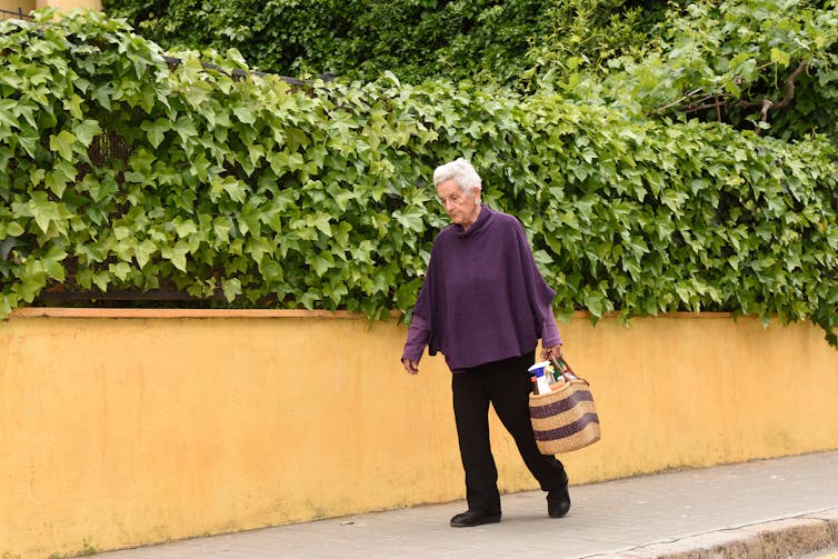 Elderly woman carries a bag of shopping as she walks down the street.