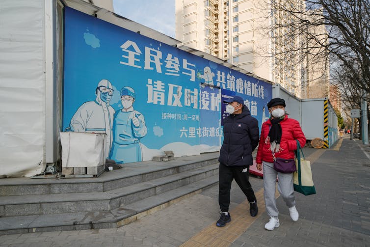 Dos personas pasan frente a un cartel de salud pública en Beijing.