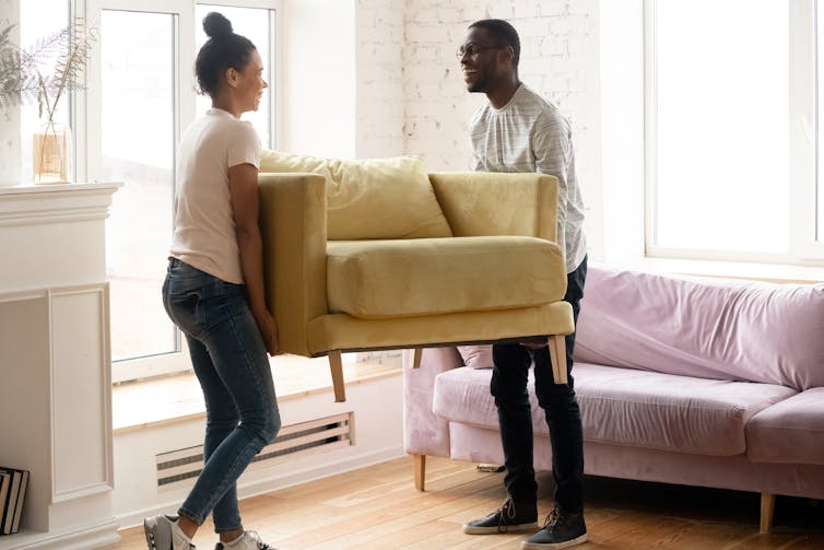 Couple lifting up sofa in living room.