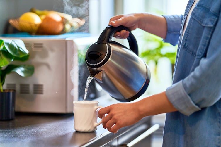 Woman pouring kettle water into mug.