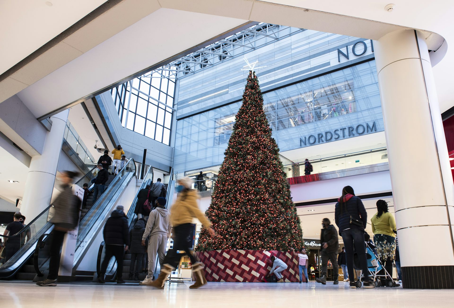 Shoppers pass a large Christmas tree with a Nordstrom store behind it.