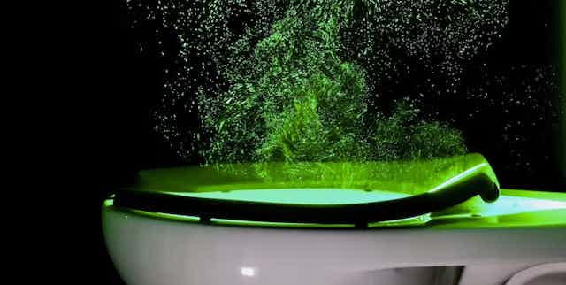 Panache de particules illuminées par un laser au-dessus d'un toilette dont la chasse est tirée