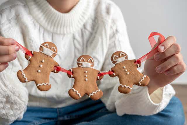 A woman holds a string of gingerbread people, decorated with masks.