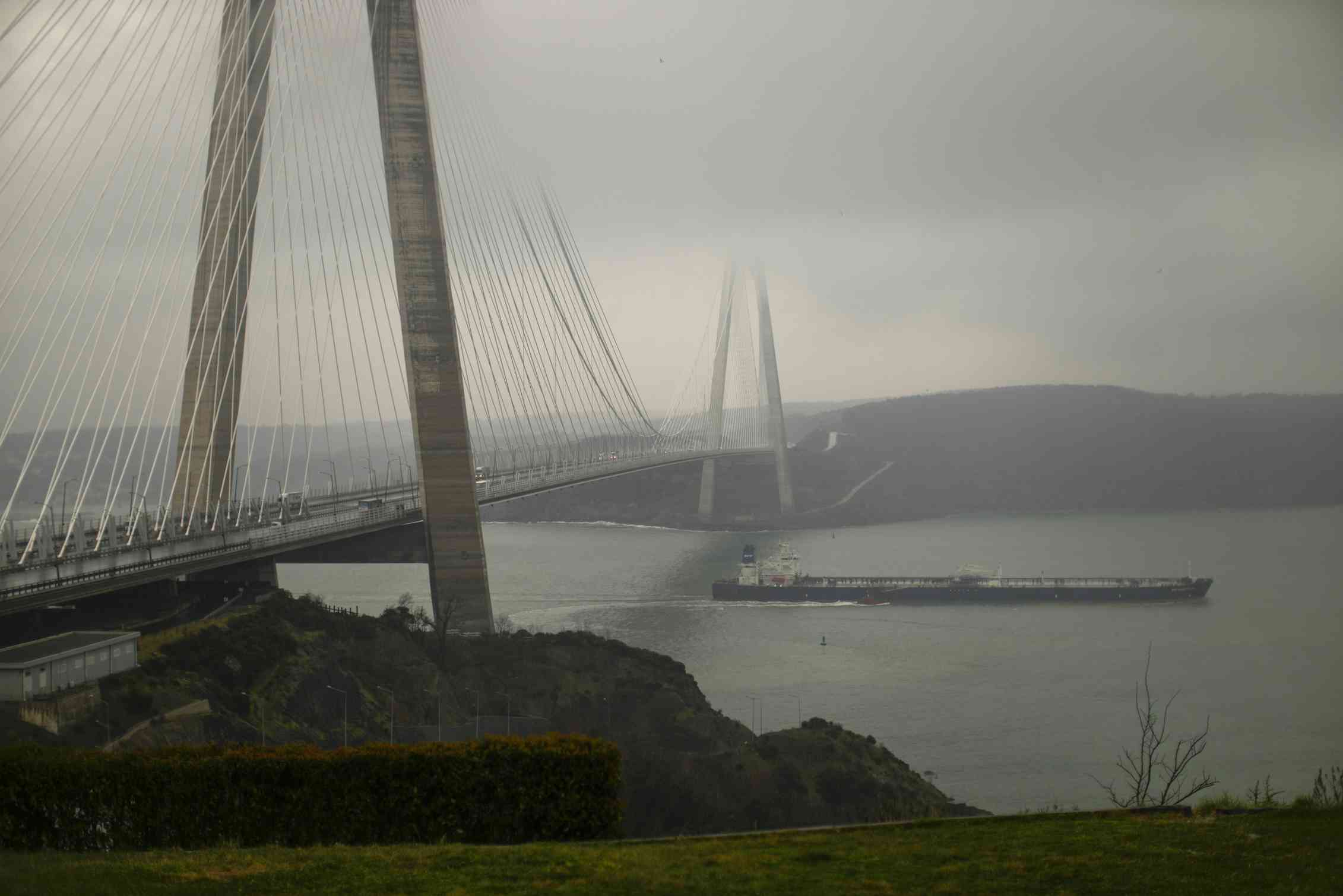 An oil tanker sails under a huge suspension bridge on a foggy day.