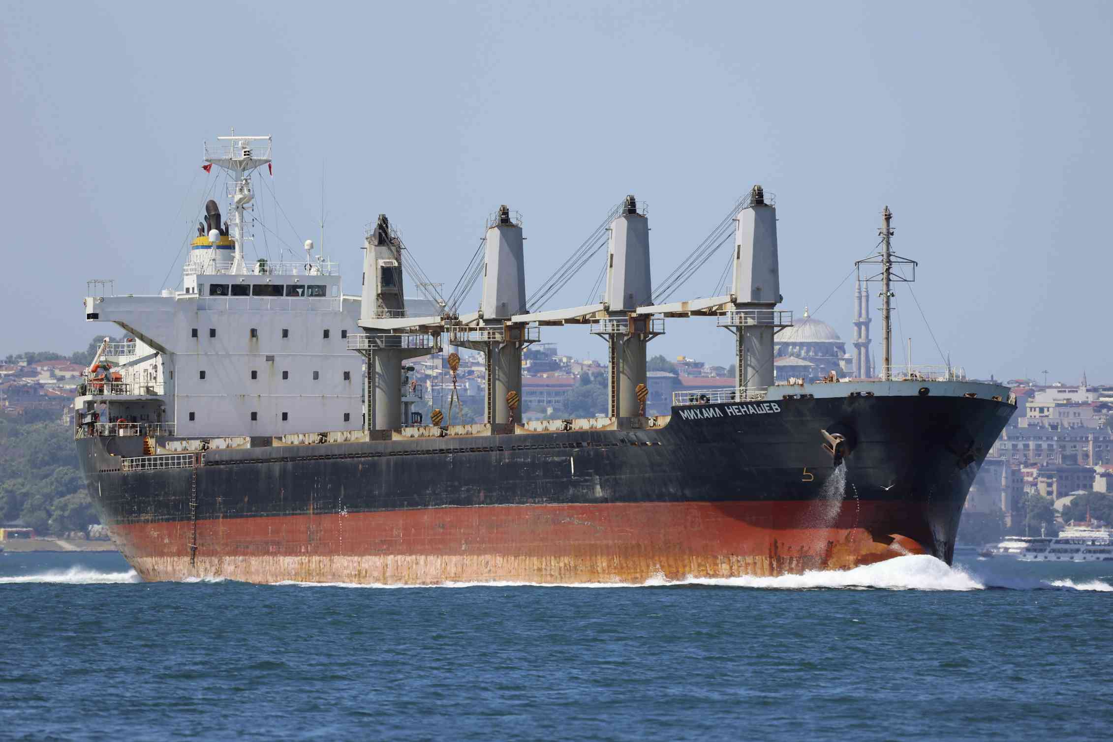 A large cargo ship with a rusty hull sails in a strait.