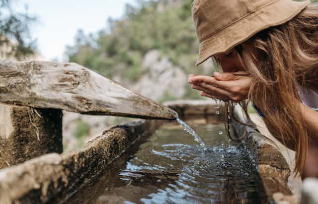 woman drinks water outdoors from old trough
