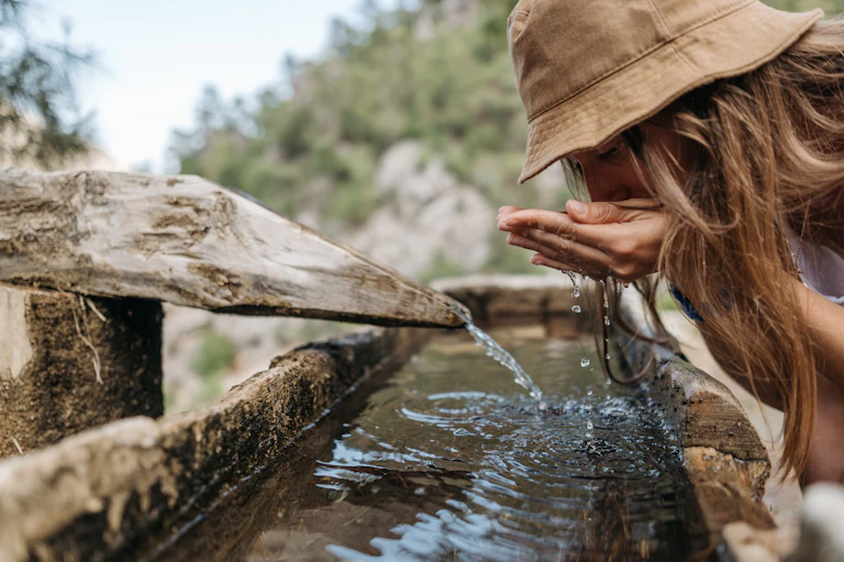 woman drinks water outdoors from old trough