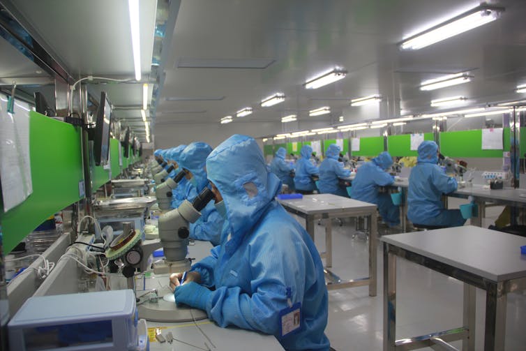 Workers wearing blue clean suits in a manufacturing plant.