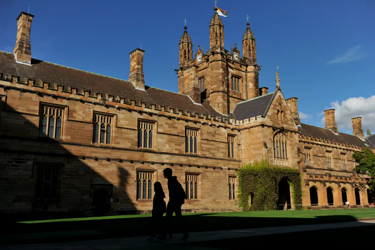 The shadows of two students against sandstone buildings at Sydney University.