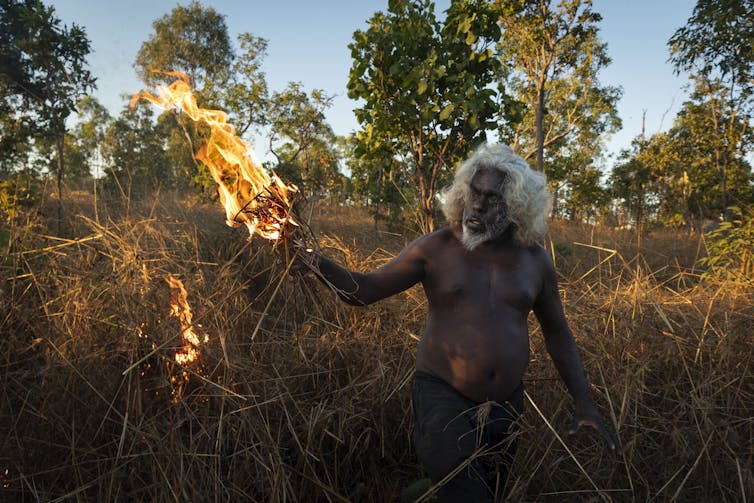 An Aboriginal man applying fire to bushland