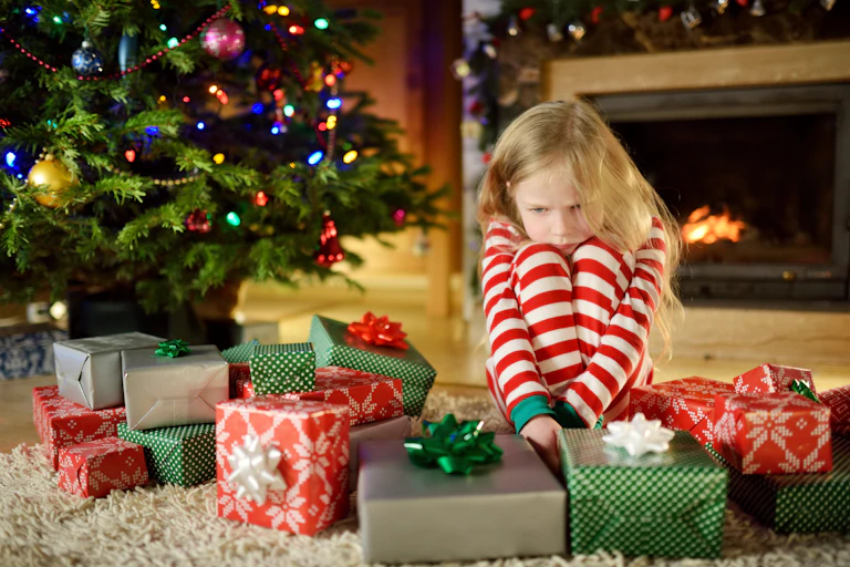 Girl child contemplating wrapped gifts besides Christmas tree.
