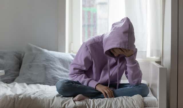 Teen in a purple hoodie sits on their bed