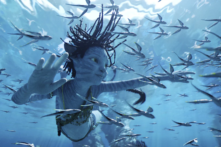 A young n'avi character swims underwater surrounded by fish.