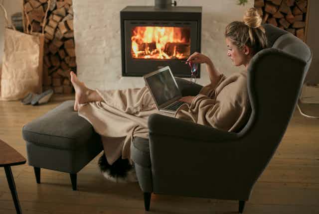 Woman sitting in front of a fire with a blanket.