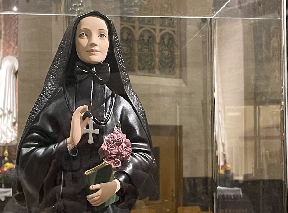 A saint's statue, dressed in all black, holding pink roses under one arm.
