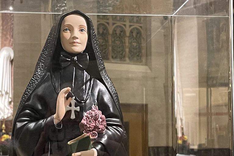 A saint's statue, dressed in all black, holding pink roses under one arm.